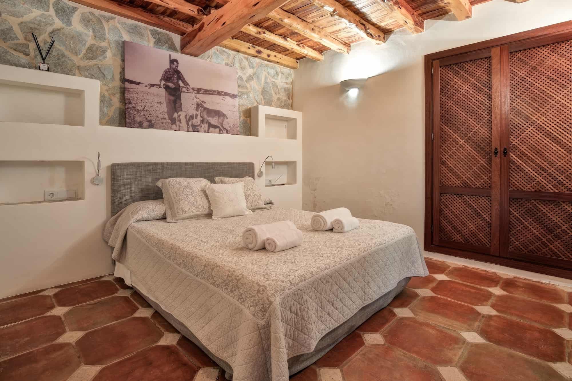 ibiza luxury villa bedroom in rustic style with historic picture above the bed and wooden ceiling beams