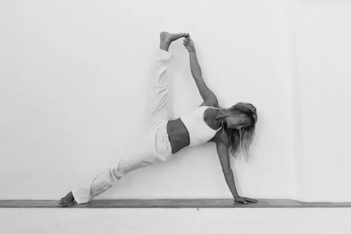 Lana Savic yoga teacher showing a yoga pose against a white wall, black and white image