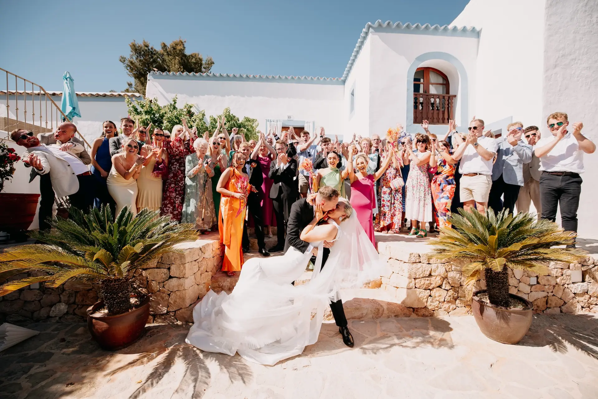olivia and samuels wedding at can frare ibiza feature image showing entire wedding party outside can frare ibiza with groom kissing his bride